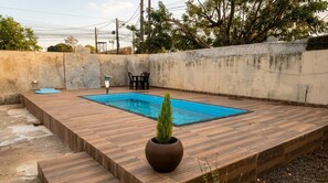A rectangular swimming pool with a wooden deck surrounding it, a potted plant, and a small table with chairs. - Vrbo Property (Foz do Iguaçu)