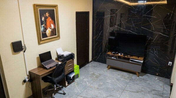 A room with a desk, chair, laptop, printer, and a large flat-screen TV on a stand. - Vrbo Property (Foz do Iguaçu)
