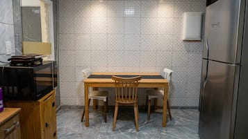 A compact kitchen with a wooden table and chairs, a microwave, a refrigerator, and a tiled backsplash.