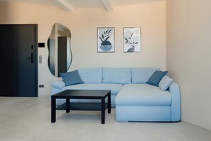 Un salon moderne avec un canapé d’angle bleu clair, une table basse de couleur foncée et deux œuvres d’art abstraites accrochées au mur.