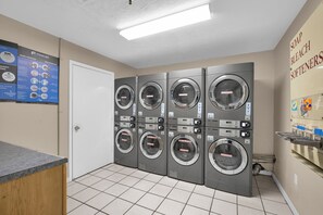A laundry facility with multiple washing machines, a detergent dispenser, and a wall-mounted instruction board. - Atlantic Sunrise-Oceanfront-Minutes from Flagler-2Bed/2Ba (New Smyrna Beach)