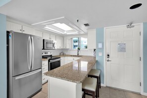 A modern kitchen with a central island, stainless steel appliances, and a view to the outside. - Atlantic Sunrise-Oceanfront-Minutes from Flagler-2Bed/2Ba (New Smyrna Beach)