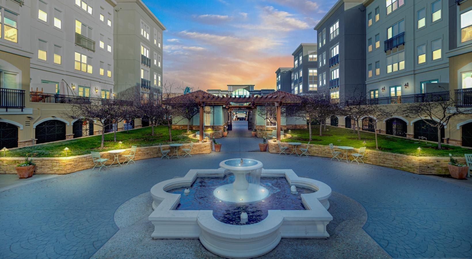 A courtyard with a central fountain, surrounded by buildings with balconies and outdoor seating.