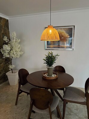 A dining area with a round table, four chairs, a hanging lamp, a framed picture, and a potted plant. - Beautiful  2-Bedroom Apartment with New Appliances & AC in Costambar beach (Costambar)