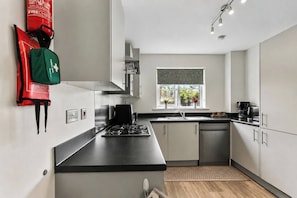 A modern kitchen with stainless steel appliances, a window with a view, and a fire extinguisher mounted on the wall. - Spacious 4BR Home | Sleeps 8 | Parking + Garden (Quedgeley)