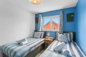 Een slaapkamer met twee bedden, een raam met gordijnen, een bureau met lamp en uitzicht op een rood gebouw.
