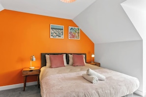 A bedroom with a sloped ceiling, a bed with a striped bedspread, two pillows, two bedside lamps, and two wall art pieces. - Spacious 4BR Home | Sleeps 8 | Parking + Garden (Quedgeley)