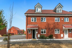 A two-story brick residential building with a red-tiled roof, multiple windows, and a white picket fence. - Spacious 4BR Home | Sleeps 8 | Parking + Garden (Quedgeley)