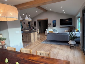 A modern kitchen with wooden cabinets, a dining area with a wooden table and chairs, a living room with a grey sofa, and a TV mounted on the wall. - Flatirons View Home Near Sundance Festival -  Private Main Floor, Boulder (Boulder)