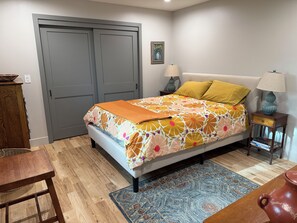 Een slaapkamer met een bed, twee bedlampen, een houten nachtkastje, een kamerkleed met een patroon en een deur.