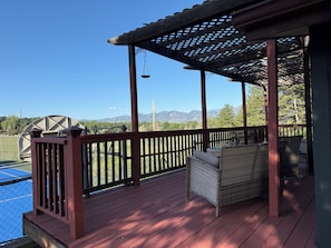 Een houten terras met rieten meubilair, een pergola en uitzicht op bergen.