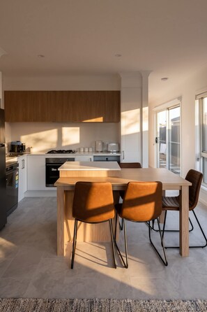 Eine moderne Küche mit einer zentralen Kochinsel, weißen Schränken und einem Essbereich mit Holztisch und Stühlen.
