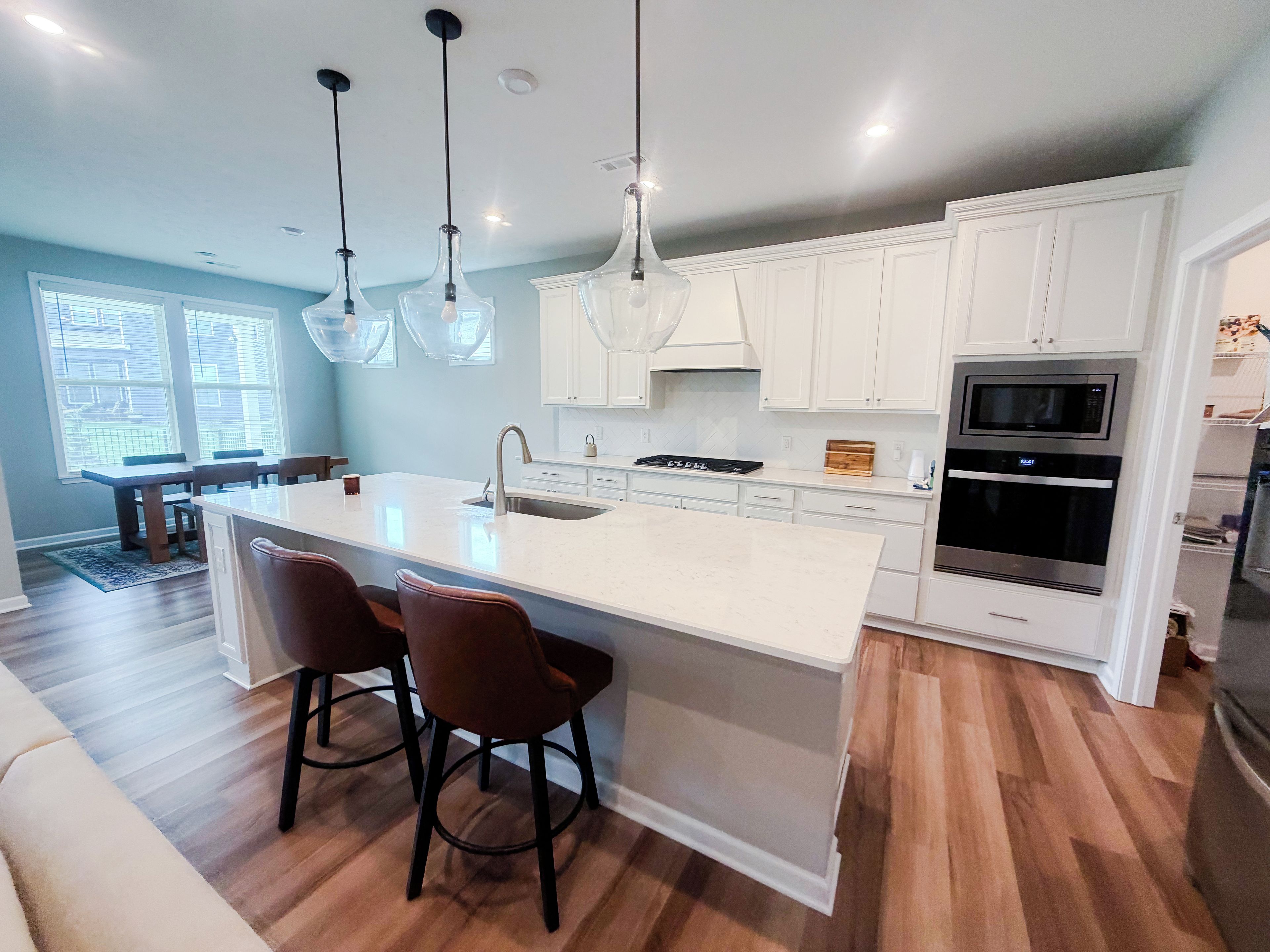 A modern kitchen with white cabinetry, a large island with bar stools, a built-in oven, and pendant lighting.