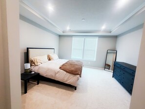 Ein Schlafzimmer mit Bett, Nachttisch, Lampe, Kommode und einem Fenster mit Jalousien.