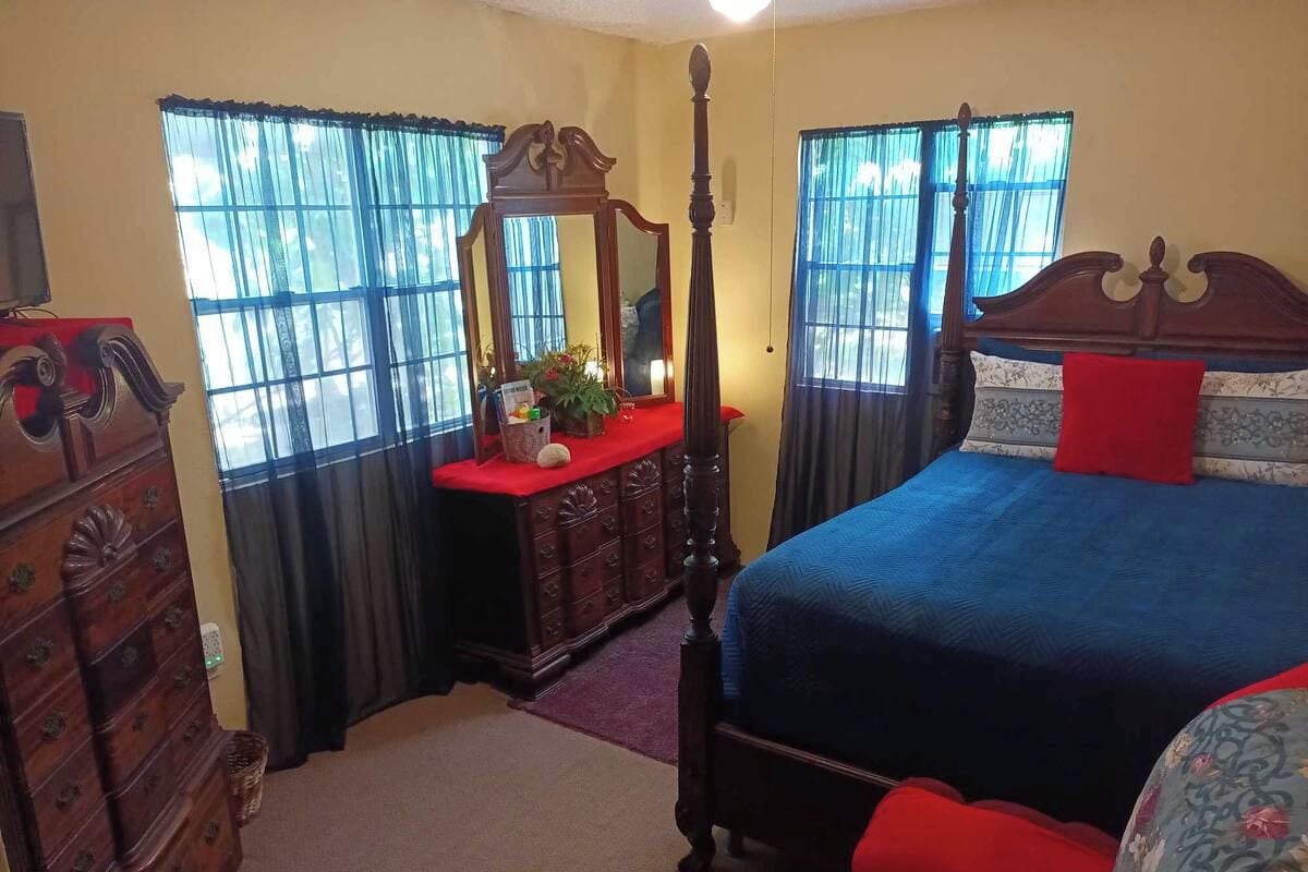 A bedroom with a four-poster bed, a dresser, a mirror, and a window with curtains.