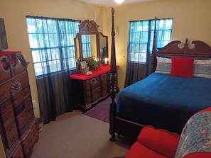 A bedroom with a four-poster bed, a dresser, a mirror, and a window with curtains. - Mahogany Getaway Herbal Healing U.SV.I. (Christiansted)