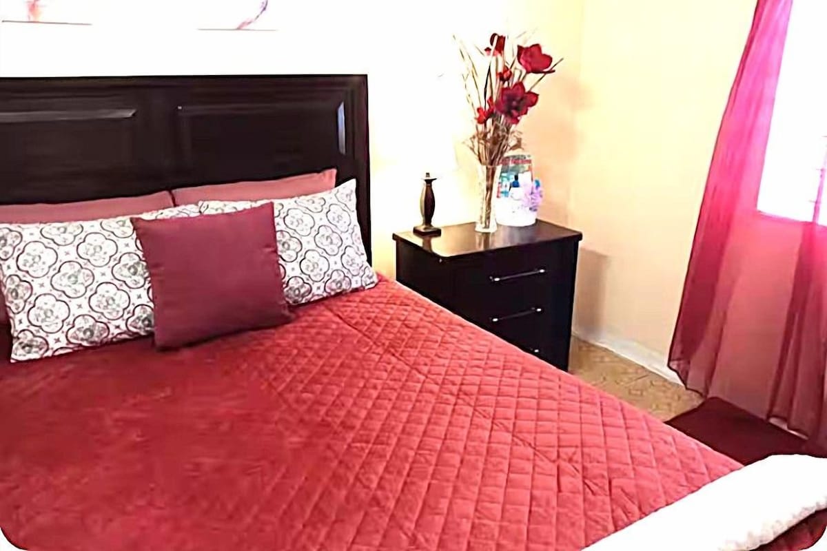 A bed with a red quilt, a dark headboard, and patterned pillows.