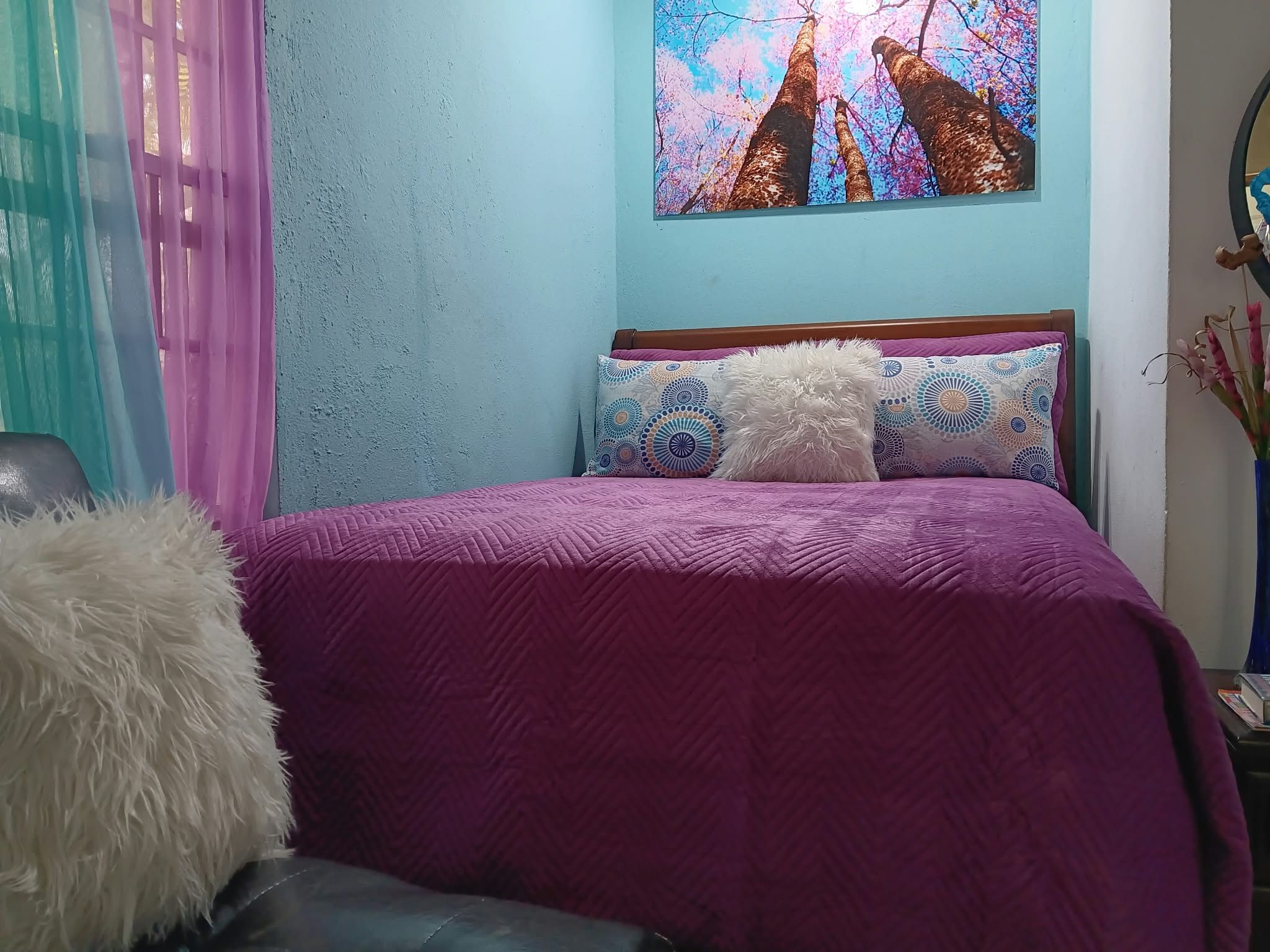 A bed with a purple bedspread, two patterned pillows, and a fluffy white pillow.