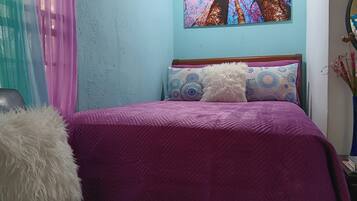 A bed with a purple bedspread, two patterned pillows, and a fluffy white pillow.