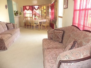 A living room with a sofa, a dining table with chairs, and a window with curtains. - Mahogany Getaway Herbal Healing U.SV.I. (Christiansted)