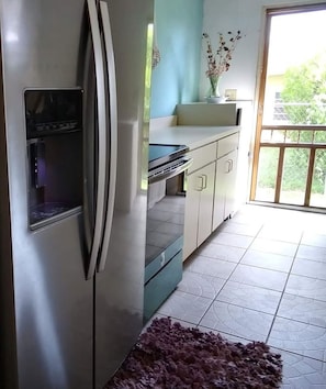 A kitchen with a refrigerator, a microwave, and a sink. There is a window with a view of greenery outside.