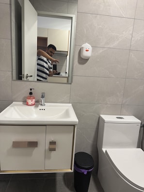 Ein Badezimmer mit weißem Waschbecken, einem Spiegel, einer Toilette und einem Mülleimer.