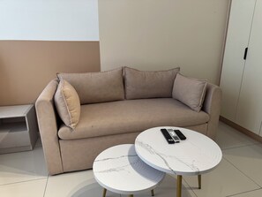 A beige sofa with a matching pillow, two round tables with marble-like patterns, and a remote control on one of the tables. - Majestic Residence KLCC by Uniquehome (Kuala Lumpur)