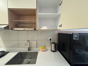 A modern kitchen with a stainless steel sink, a black refrigerator, and a wooden shelf above the sink. - Majestic Residence KLCC by Uniquehome (Kuala Lumpur)
