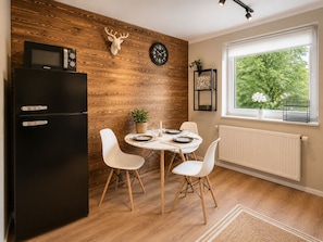 Eine moderne Küche mit einem schwarzen Kühlschrank, Holzvertäfelung, einer Uhr und einem Fenster mit Blick auf Bäume.