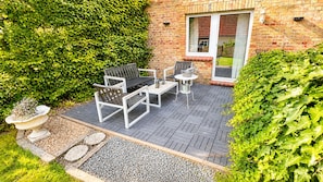 An outdoor patio with a brick wall, a white bench, a table, and a chair. - Vrbo Property (Adenbüttel)