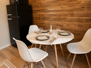 A dining area with a round table set for four, white chairs, a black refrigerator, and a wooden wall. - Vrbo Property (Adenbüttel)