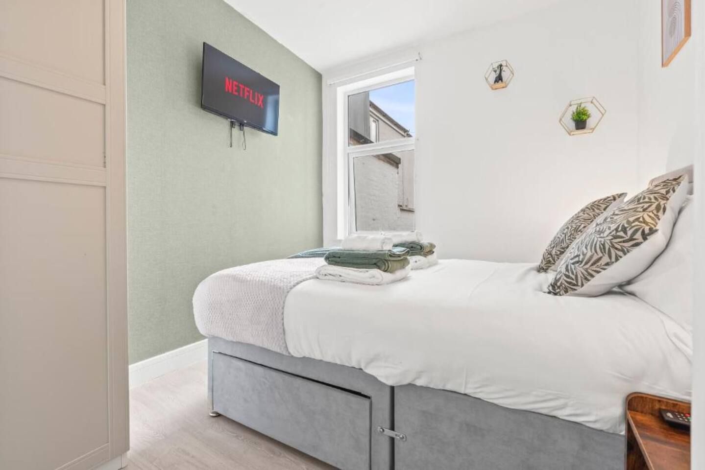A bedroom with a bed, a television mounted on the wall, a window, and a door.
