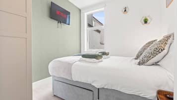 A bedroom with a bed, a television mounted on the wall, a window, and a door.