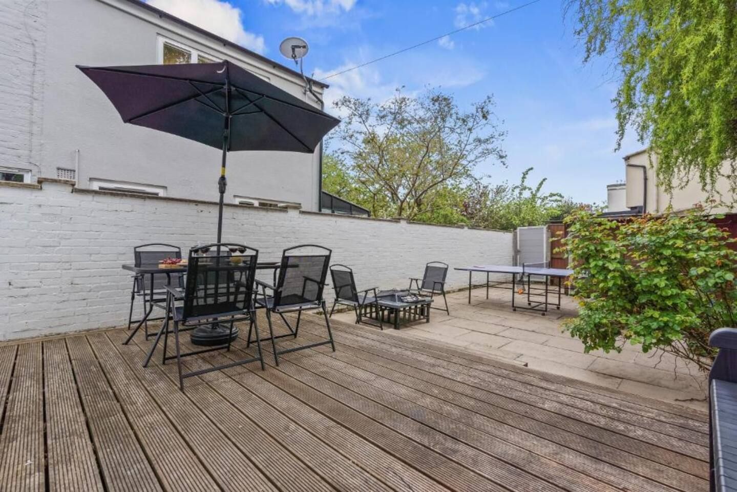 An outdoor patio with a table and chairs, a ping pong table, and a satellite dish on a white building.