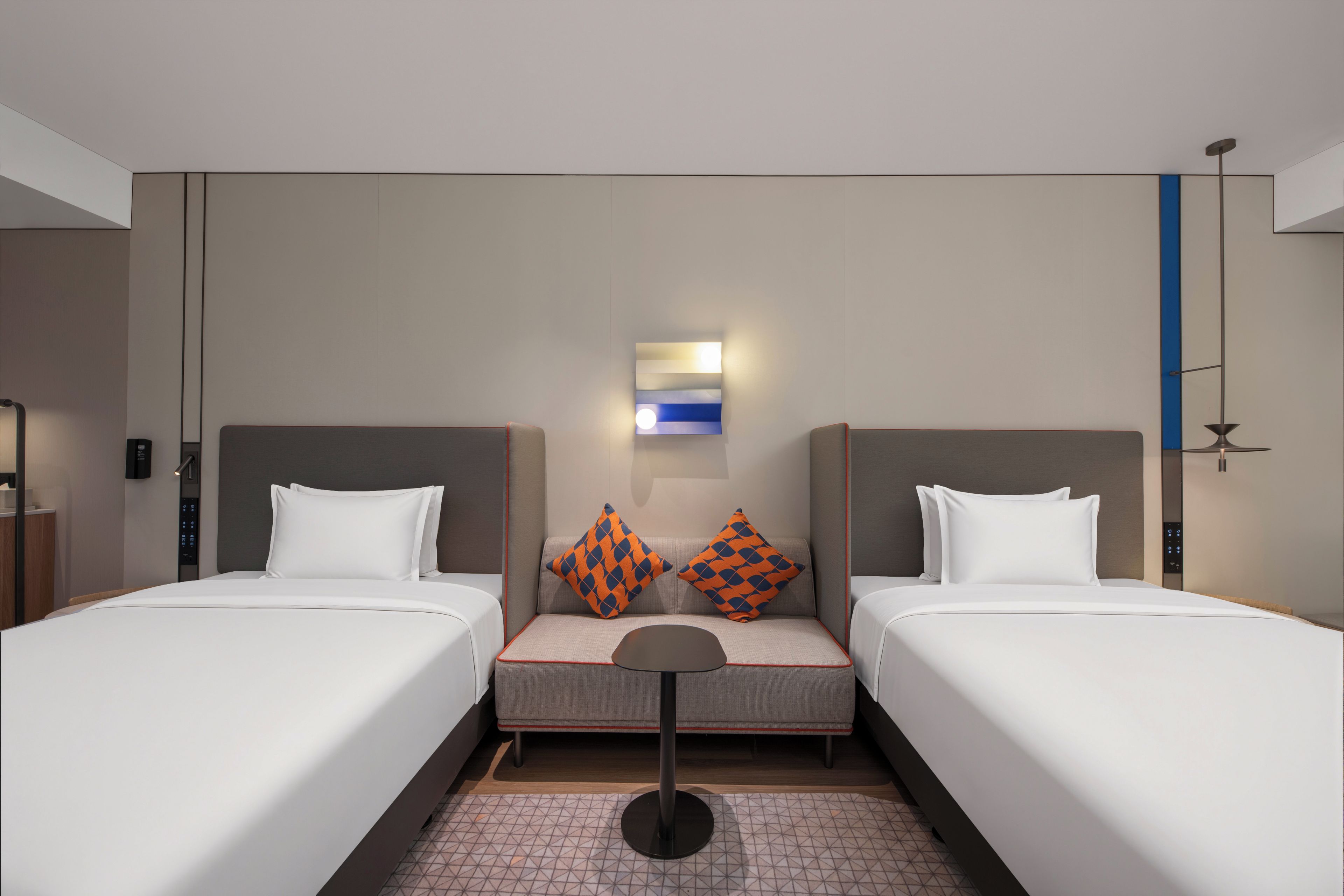 Een hotelkamer met twee bedden, een tafeltje en een wandlamp.