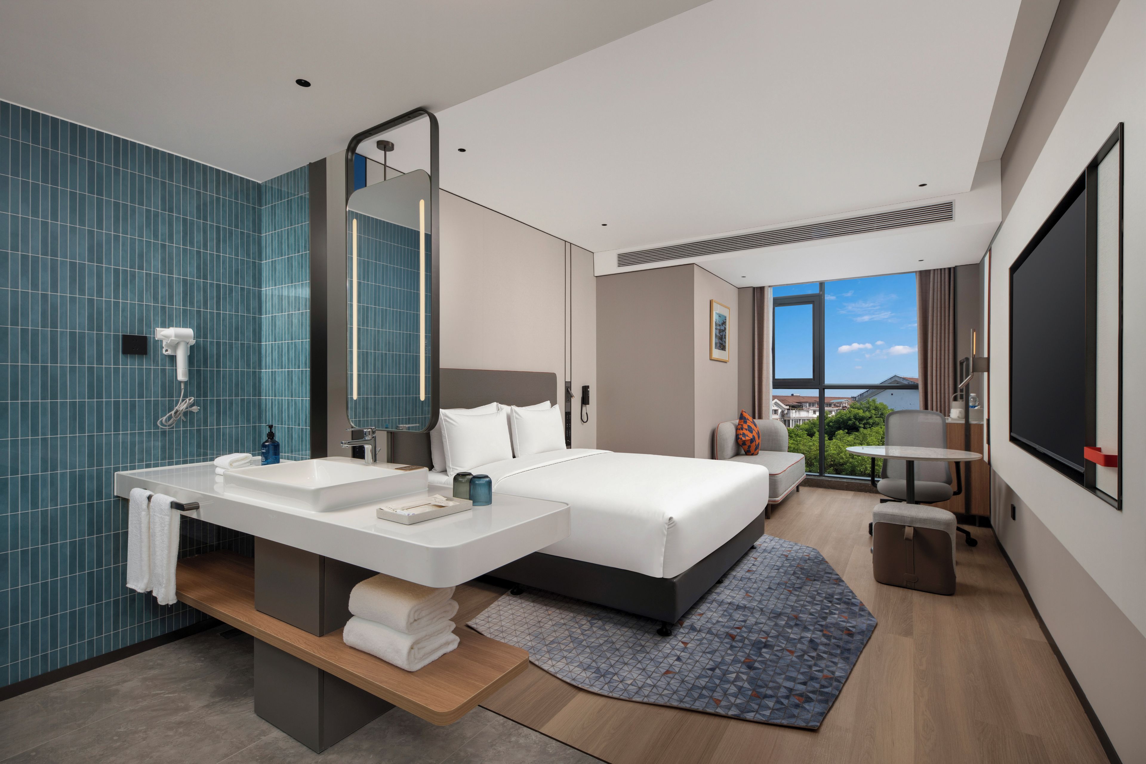 Una camera d'albergo moderna con un letto grande, un'area salotto separata, un bagno con uno specchio ampio e vista sull'esterno.