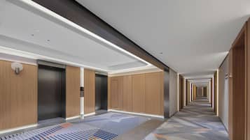 A modern hotel corridor with a patterned carpet, wooden panel walls, and a long hallway.