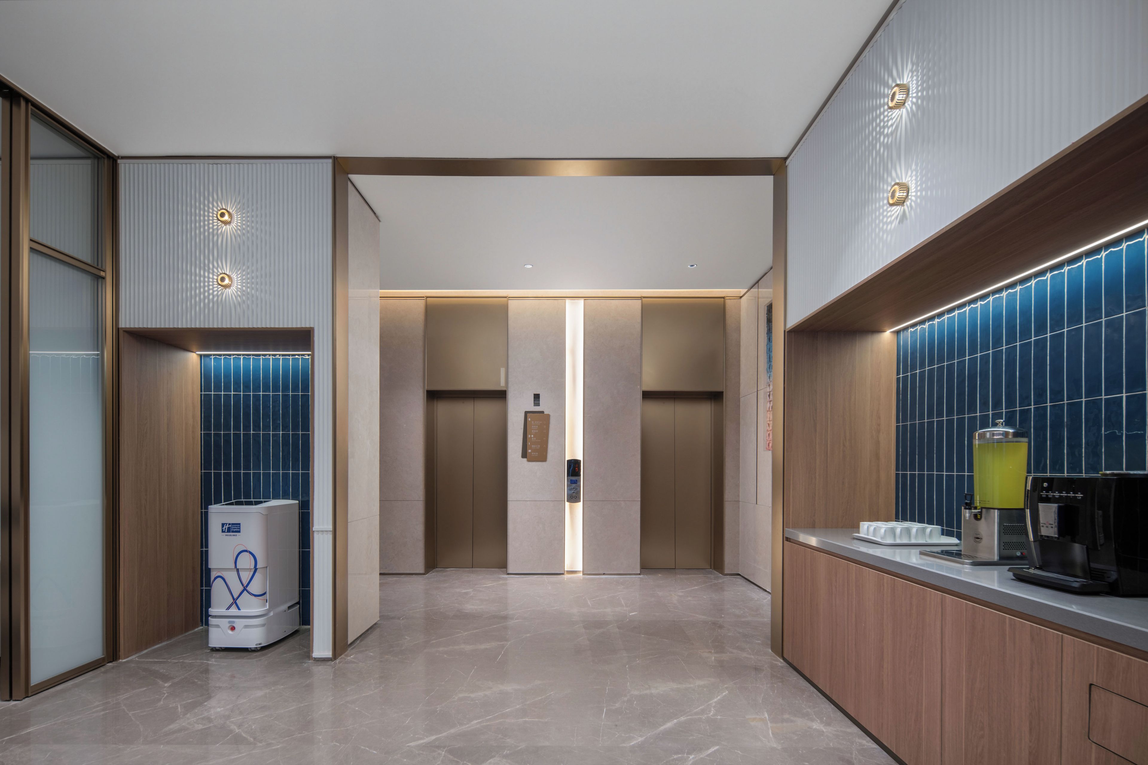Een moderne liftruimte met een centrale liftdeur, een waterdispenser en een koffieapparaat aan de rechterkant.
