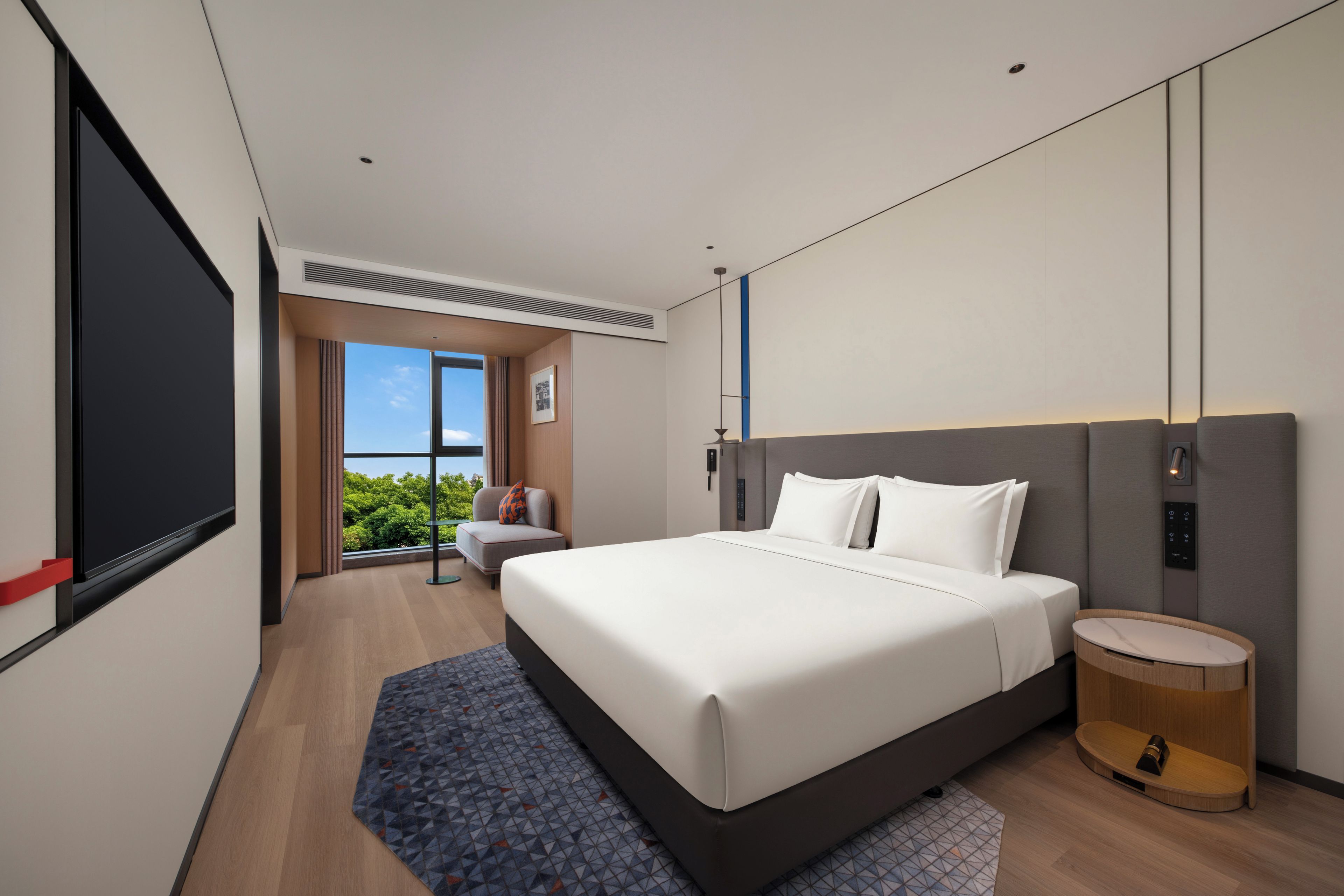 Een moderne hotelkamer met een groot bed, een nachtkastje, een wandtelevisie en een raam met uitzicht op groen.