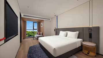 Een moderne hotelkamer met een groot bed, een nachtkastje, een wandtelevisie en een raam met uitzicht op groen.