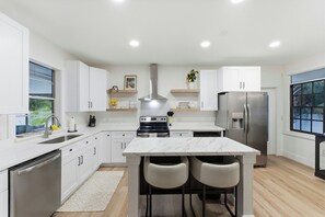 A modern kitchen with white cabinetry, a central island with chairs, stainless steel appliances, and a window with a view. - Sanford Pool and Patio Retreat (Sanford)