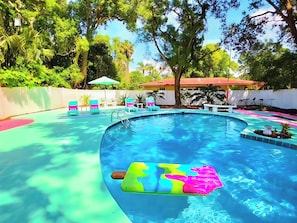 A swimming pool with a colorful floating mat, surrounded by trees and a white fence. - Sanford Pool and Patio Retreat (Sanford)