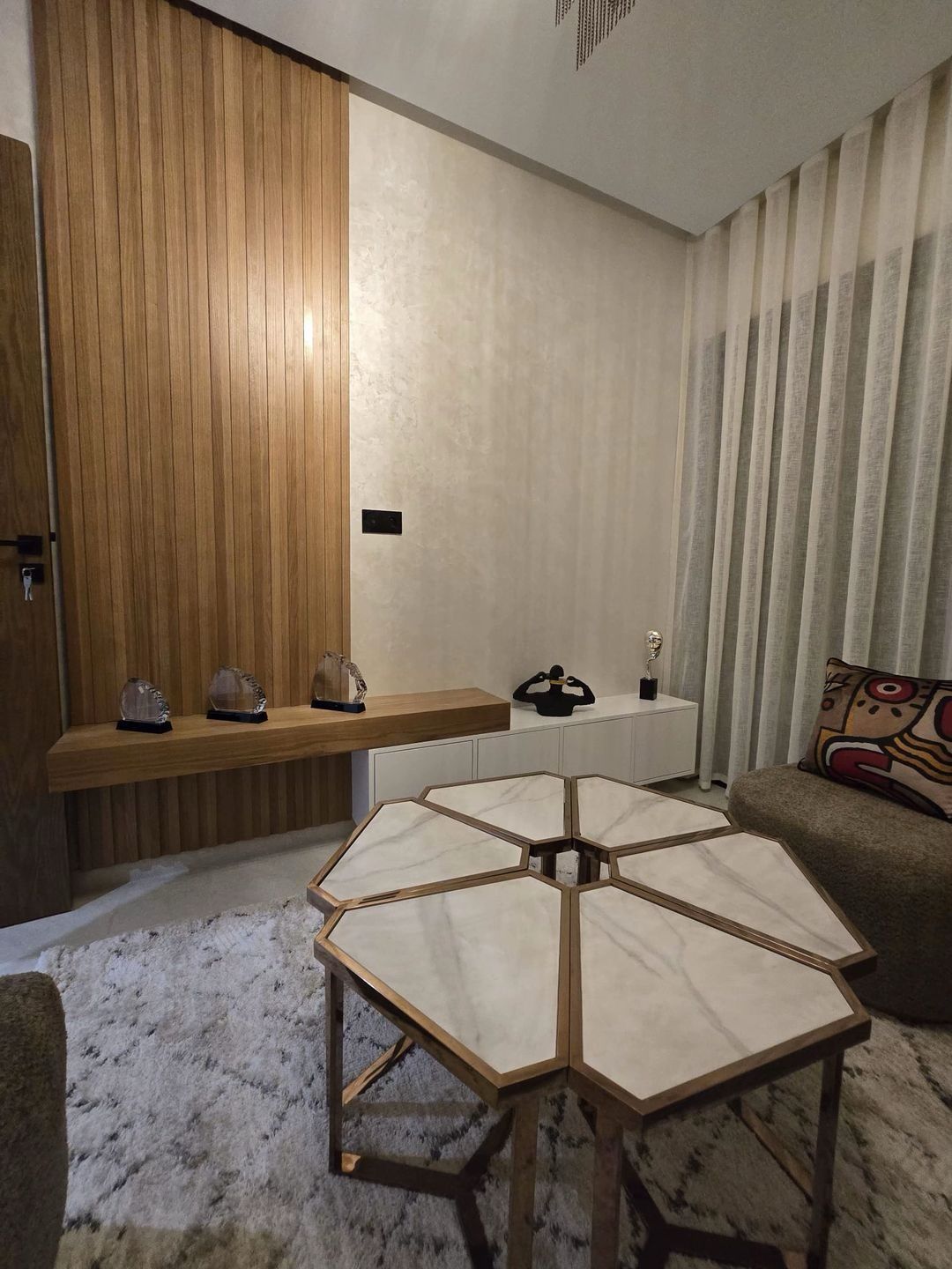 Un salón moderno con una mesa de centro hexagonal, un panel de pared de madera y un sofá con un cojín estampado.