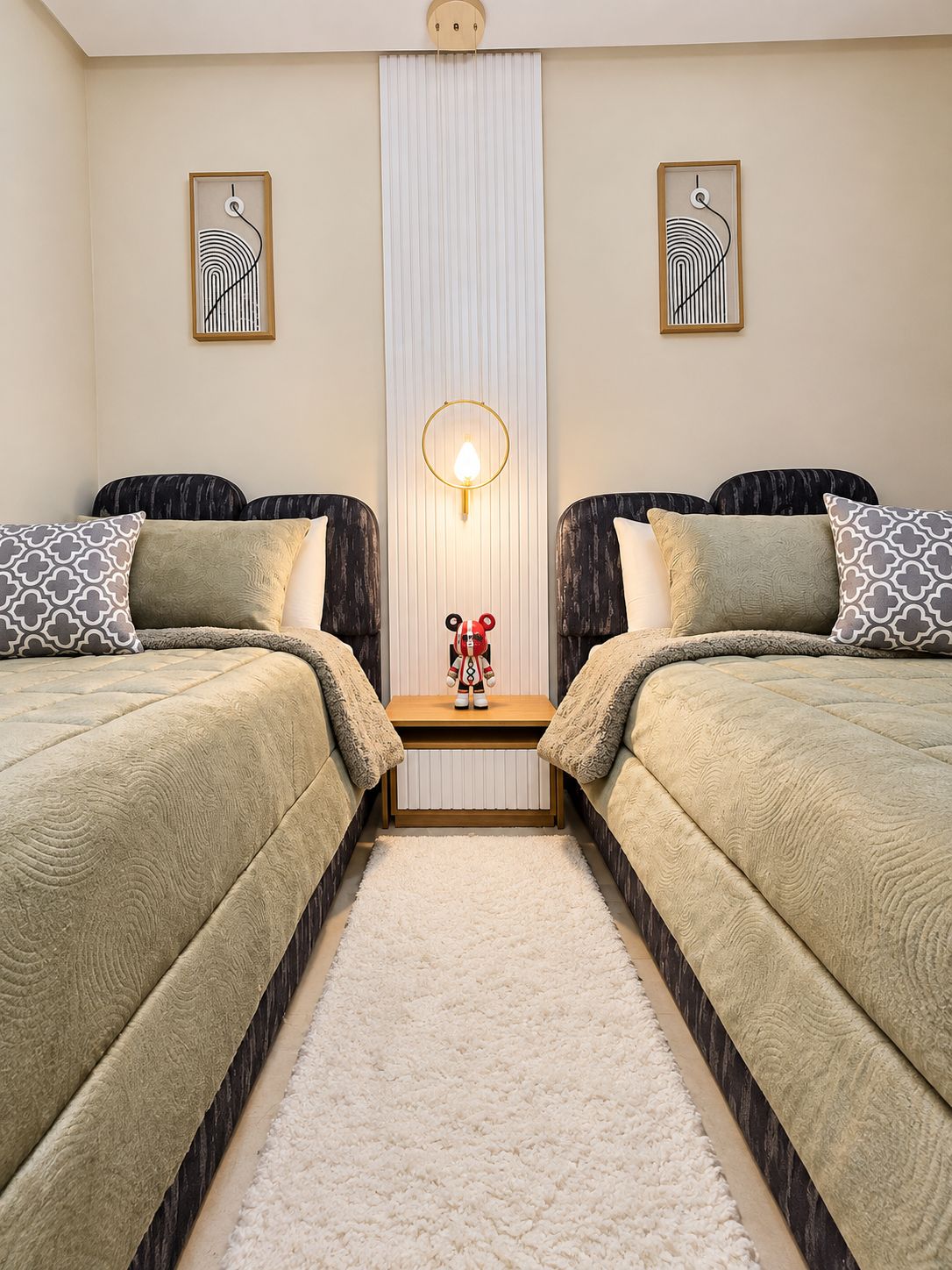 A hotel room with two beds, a central nightstand with a lamp, and two wall-mounted artworks.