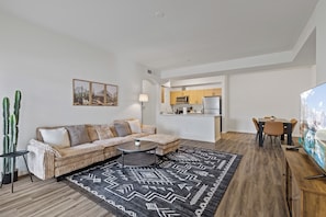A modern living room with a sofa, coffee table, and a dining area with chairs and a TV. - Desert Bloom Retreat • Peaceful 1BR Oasis (Mesa)