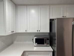 Une cuisine avec des meubles blancs, un four à micro-ondes en acier inoxydable et un réfrigérateur.