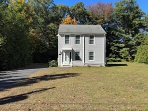 A two-story house with a front porch, surrounded by trees and a grassy yard. - Cozy house on one acre land with great privacy. 20 miles away from Boston (Framingham)