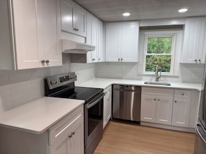 A modern kitchen with white cabinetry, stainless steel appliances, and a window providing natural light. - Cozy house on one acre land with great privacy. 20 miles away from Boston (Framingham)