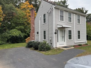 A two-story house with a brick chimney, a front door, and a small porch. - Cozy house on one acre land with great privacy. 20 miles away from Boston (Framingham)