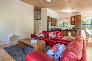 A modern living room with a red leather sofa, a wooden coffee table, and a kitchen in the background. - The Tasting Room by Waiheke Pure, close to wineries, great valley views (Auckland)